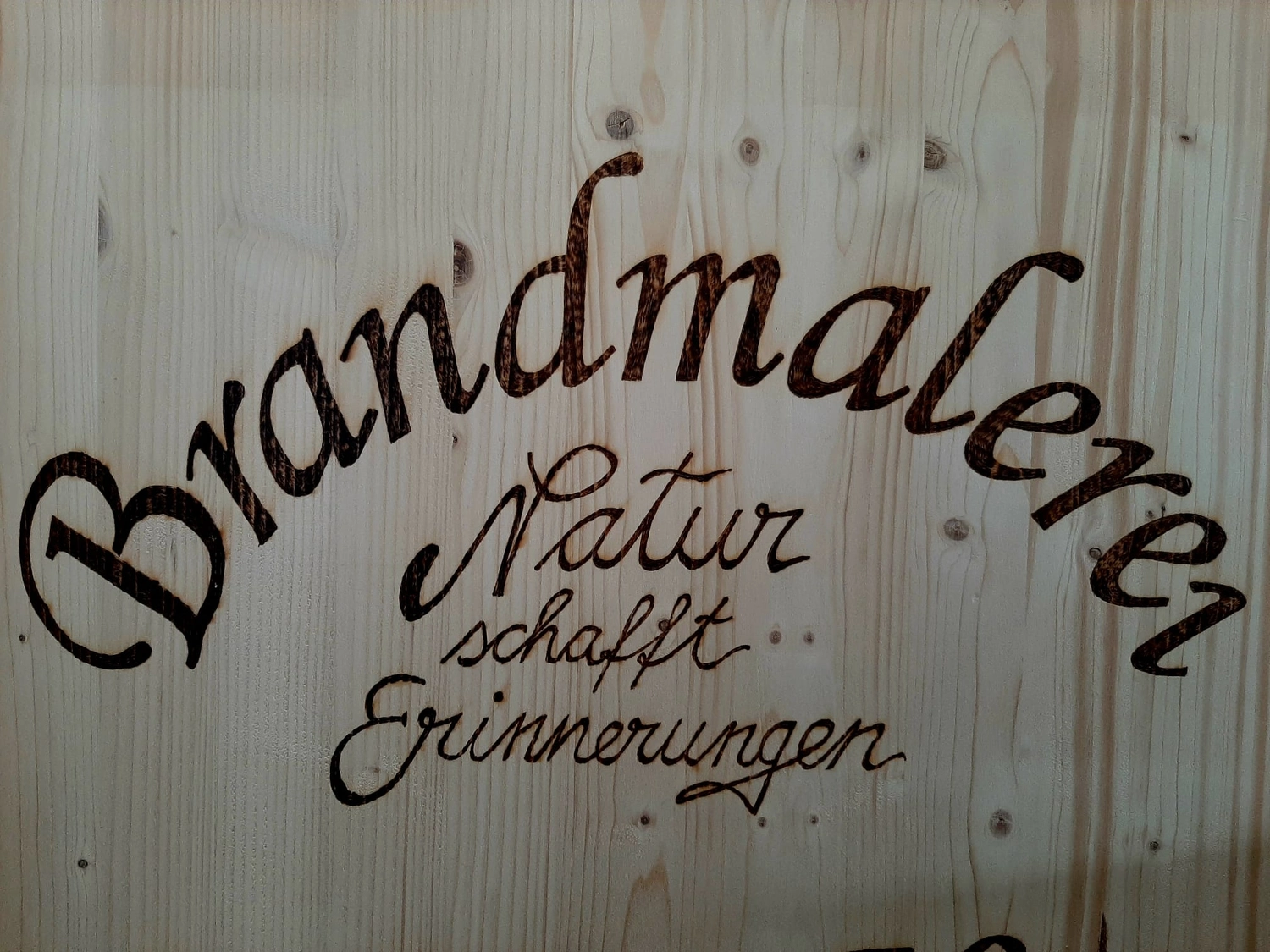 NaturTeller – vegane Ernährungsberatung - Nahaufnahme eines Brandmalerei-Kunstschildes mit dem Wort „Brandmalerei“ in einem Bogen darüber. Darunter steht der Text „Natur schafft Erinnerungen“